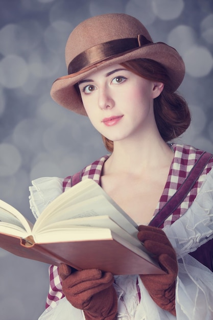 本を持つ美しい赤毛の女性。背景にボケ味のあるレトロなスタイルの写真。