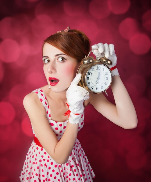 Beautiful redhead women with clock. Photo in retro style with bokeh at background.