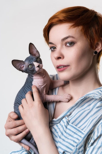 Beautiful redhead young woman holding Canadian Sphynx Cat in hands and looking away