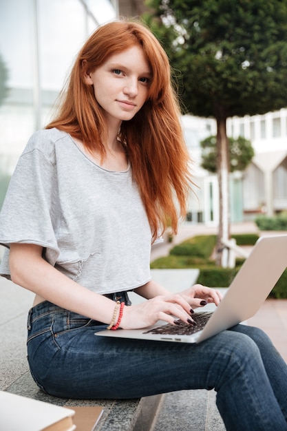 Beautiful redhead young woman sitting and using laptop outdoors