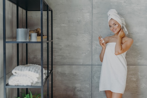 Beautiful relaxed woman wrapped in towel applying face cream