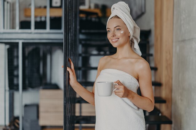 Beautiful relaxed woman wrapped in towel drinking tea