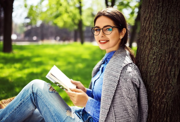 太陽が輝いている芝生で本を読んで美しいリラックスした若い女性