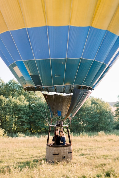 Bella romantica coppia caucasica innamorata che abbraccia nel cesto della mongolfiera colorata durante il tramonto estivo, celebrando fidanzamento o anniversario di matrimonio