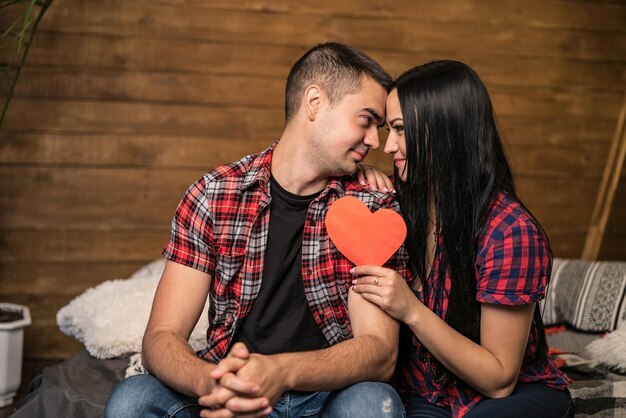 Beautiful romantic couple on wooden wall background Attractive young woman and handsome man are hugging with red heart in hands Saint Valentine's Day concept