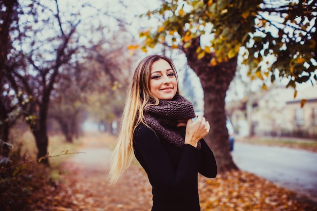 Beautiful romantic girl spinning outdoors and enjoying autumn nature Woman wears black dress and warm knitted scarf