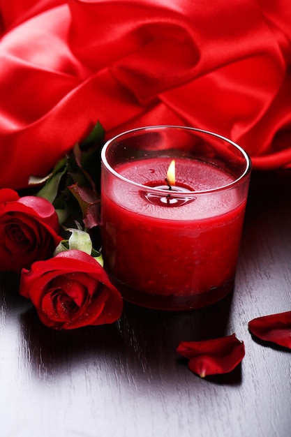 Beautiful romantic red candle with flowers and silk cloth, close up