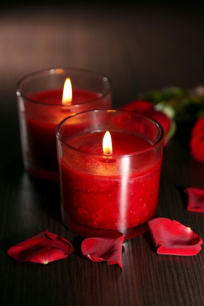 Beautiful romantic red candles with flower petals on dark wooden background