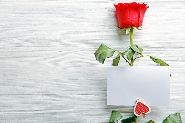 Beautiful rose with gift card on wooden background