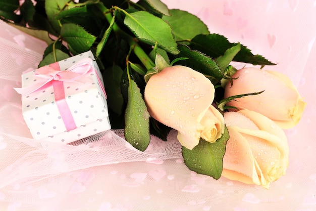 Beautiful roses and gift on pink cloth, close up