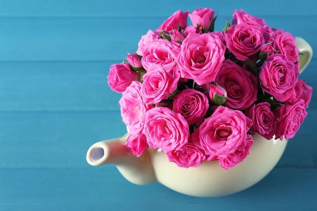 Beautiful roses in teapot on wooden background