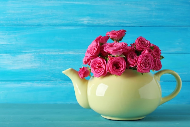 Photo beautiful roses in teapot on wooden background