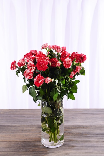 Beautiful roses in vase on table on light background