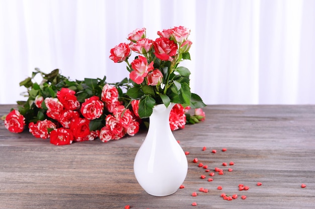 Beautiful roses in vase on table on light background