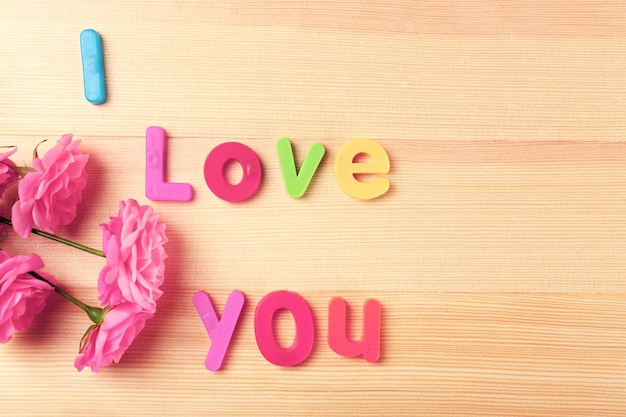 Beautiful roses with word LOVE on wooden background