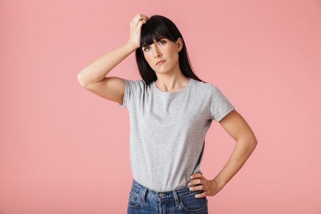 a beautiful sad displeased woman with headache posing isolated over light pink wall wall.