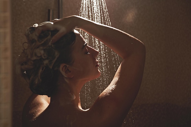 Foto bella donna europea soddisfatta lava via lo shampoo dai capelli in bagno, fa la doccia e si diverte, sorridendo