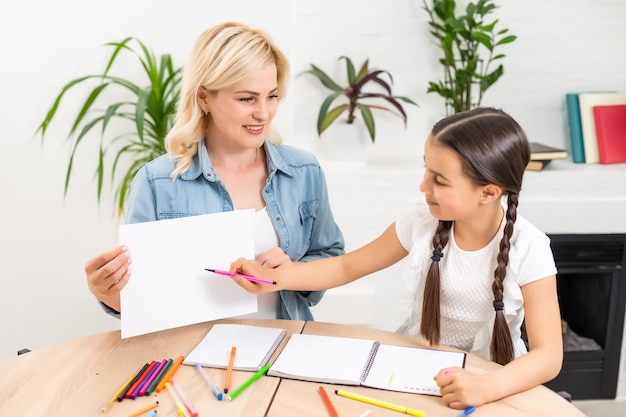 Beautiful school girl doing homework with mother at home.