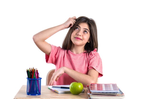 A beautiful school girl sits at the desk with apple and thinking White