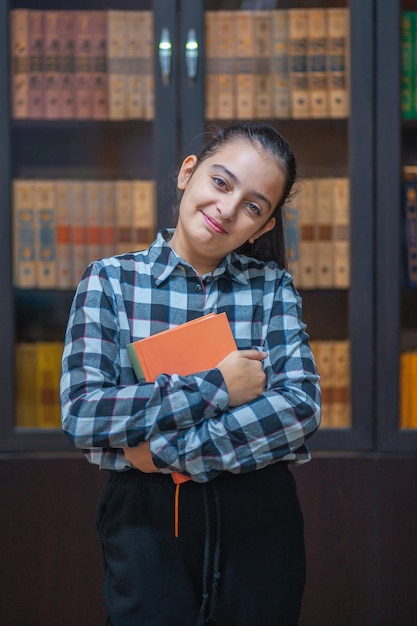 Foto una bella scolaressa che legge un libro in biblioteca.