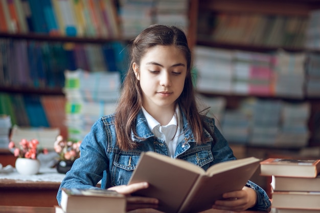 Beautiful schoolgirl sitting in the library and reading a book, education