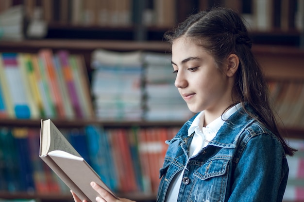 Beautiful schoolgirl sitting in the library and reading a book, education