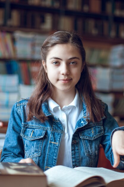 Photo beautiful schoolgirl sitting in the library and reading a book