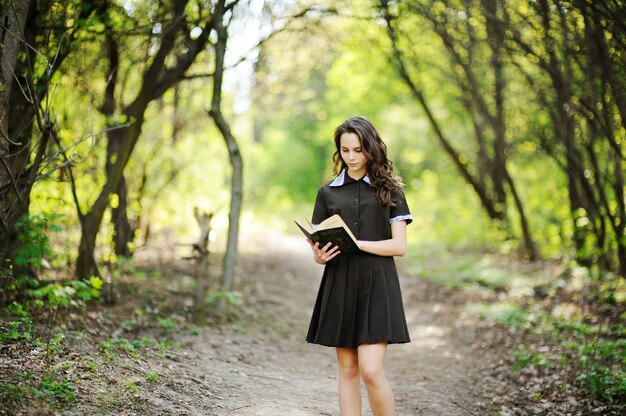 Beautiful schoolgirl with a book in hands on a background of green trees