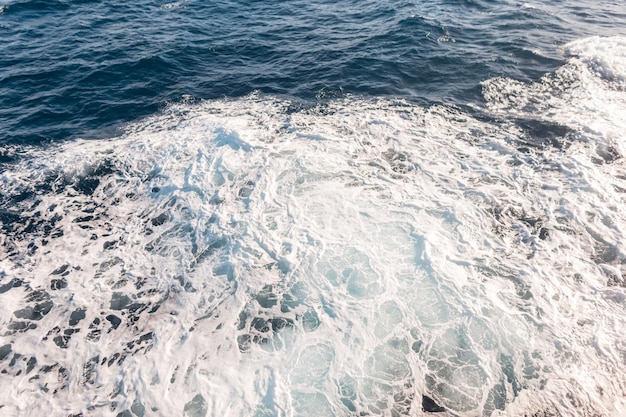 Красивая текстура морской голубой воды с волнами и видом сверху на пену