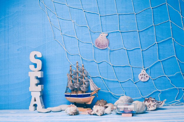 Beautiful sea composition with toy sailboat, seashell, glass bottle and fishing net on blue background