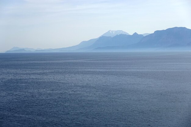 Beautiful sea landscape in soft colors with calm sea and high mountains covered with light haze