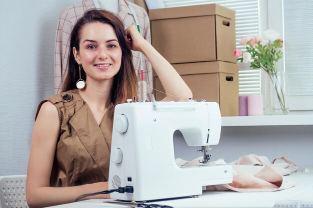 beautiful seamstress with long hair writes in a notebook. the tailor creates a collection of outfits. young woman designer clothes notes ideas in notebook