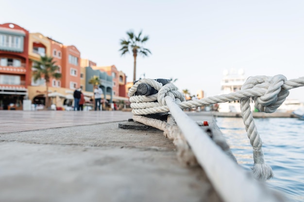 Beautiful seaport with houses, cafes, shops, people and palm\
trees. yacht is tied with a rope to a metal bollard, close-up.\
ships are moored. insurance and protection concept