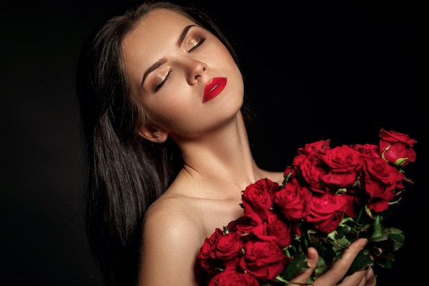 Beautiful seductive woman holding large bouquet of red roses