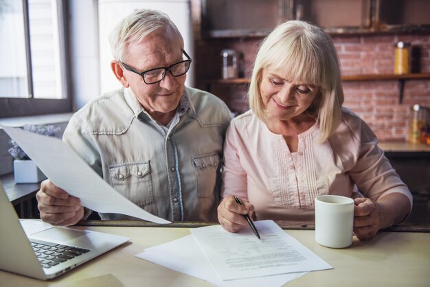 beautiful senior business couple is studying documents using a laptop and smiling while working