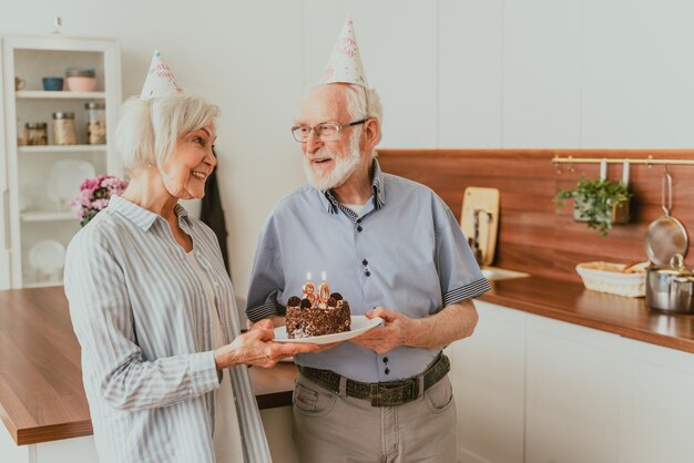 バースデーケーキで記念日を祝う美しい老夫婦-自宅で誕生日パーティーを開く老夫婦