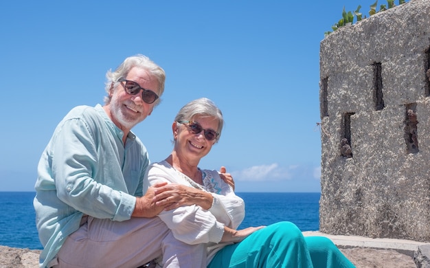 Красивая старшая пара обнимается на море, наслаждаясь летними каникулами, глядя в камеру