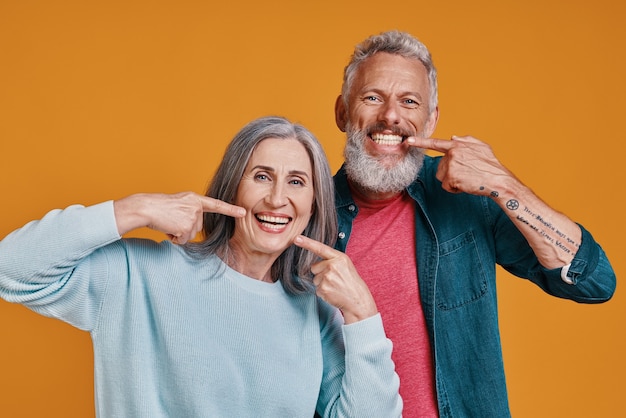 beautiful senior couple looking at camera and pointing their teeth with smile