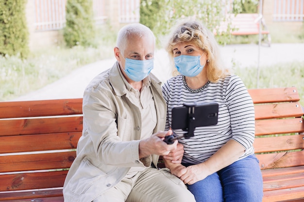 Красивая пара старших в любви носить медицинскую маску и делая selfie снаружи