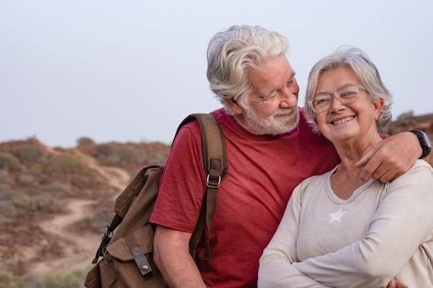 写真 夕焼けの光で田舎を歩いて、幸せそうに笑って美しい年配のカップル。屋外と自然を楽しんで抱き締める妻と夫の白い髪の老夫婦