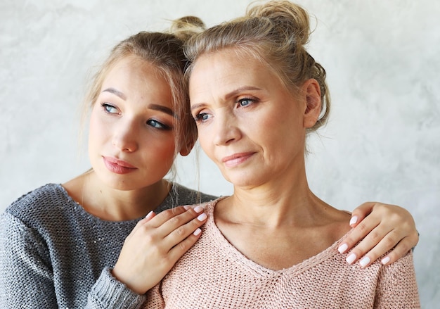 Beautiful senior mom and her adult daughter are hugging looking at camera and smiling At Home