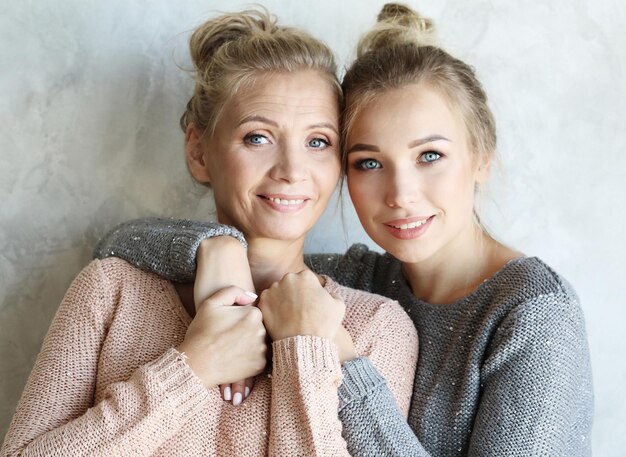 Beautiful senior mom and her adult daughter are hugging looking at camera and smiling