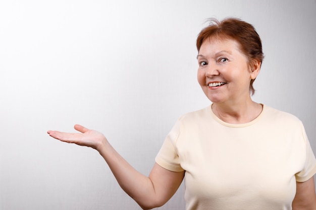 Beautiful senior woman shows a hand to the side on white in a light T-shirt