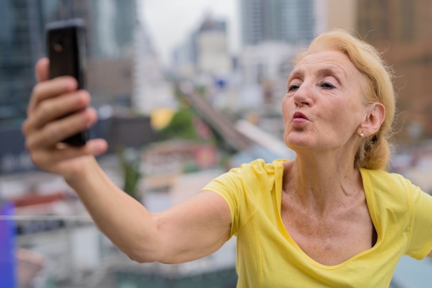 Beautiful senior woman taking selfie with mobile phone in city