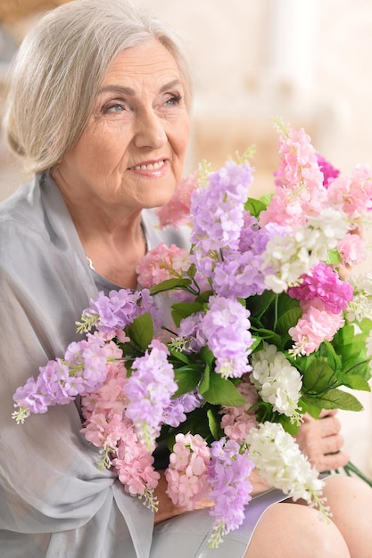 Красивая старшая женщина с букетом цветов в светлой комнате