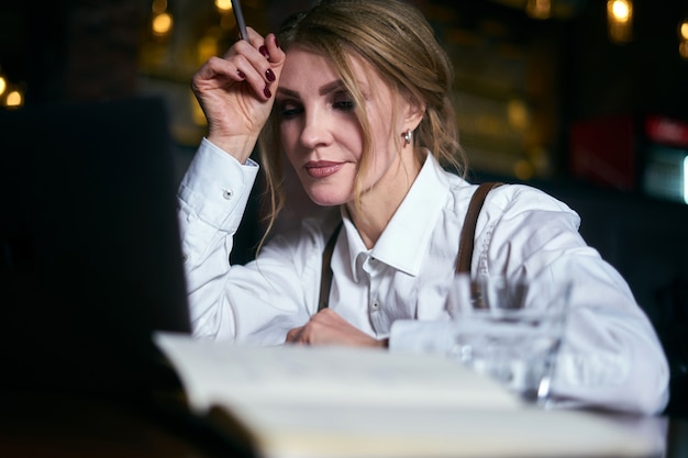 Foto bella donna senior che lavora in caffè con il computer portatile e che scrive in blocco note