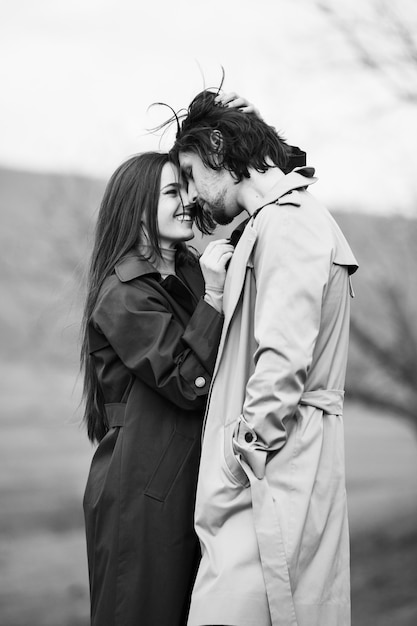 Beautiful sensual portrait of young stylish couple in love Image of adorable brunette couple in rain trench coat in park