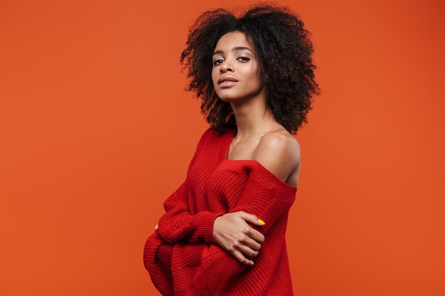 Beautiful sensual young african woman wearing sweater standing islolated over red wall