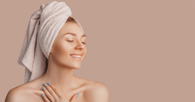 Beautiful sensual young girl with clean skin on a beige background with a mockup. Topless woman in a towel. The concept of spa treatments, natural beauty and care, youth, cream and mask, freshness