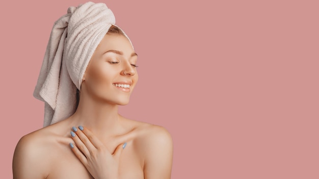 beautiful sensual young girl with clean skin on a pink background with a mockup. topless woman in a towel. the concept of spa treatments, natural beauty and care, youth, cream and mask, freshness